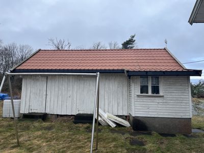 Fotografi av en liten, hvit malte hytte med rødt tak sett fra siden.