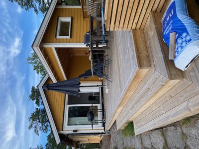 Fotografi av en gul hytte med en treterrasse og en blå paraply.