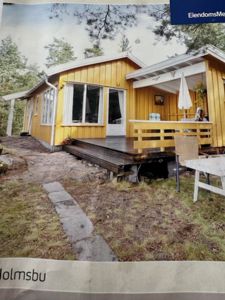 Fotografi av en gul hytte med en terrasse og omgivelser.