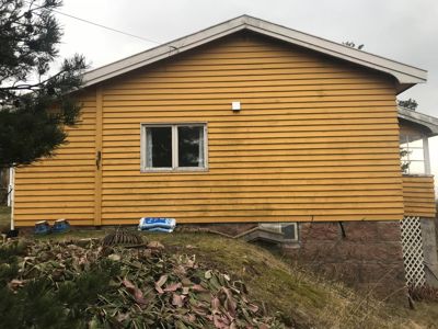 Fotografi av en gul, trepanelert bygning sett fra siden.