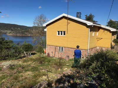 Fotografi av en gul fasettbygning med steinfot, sett fra siden med utsikt over vann.