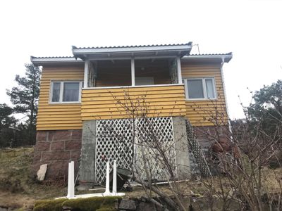 Fotografi av en gul fasettvegg med steinfundament, sett fra foran.