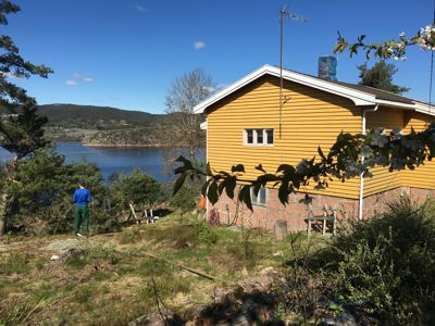 Fotografi av en gul hytte ved vannet med en person i forgrunnen.