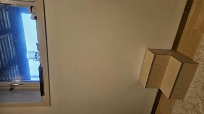 Fotografi av en vegg med et vindu og en trekonstruksjon (kanskje en sokkel eller trappetrinn) i en innendørs setting.