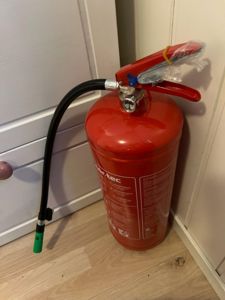 Fotografi av en rød brannslukker som står i et hjørne på et gulv.