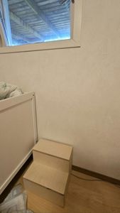 Fotografi av en innendørs hjørne i et rom, med en liten trapp, en seng og et vindu.