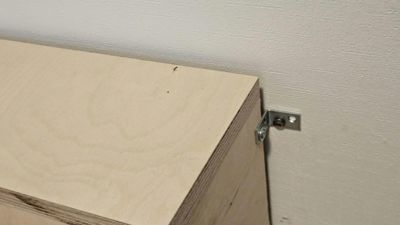 Fotografi av en detalj i en bygning, som viser en trekonstruksjon (sannsynligvis et skap eller panel) festet til en vegg med en metallbeslag.