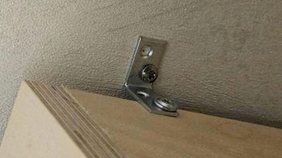 Fotografi av en metallbeslag (sannsynligvis en hengsel eller festemekanisme) montert på en vegg over en dør eller panel.