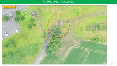 Luftfoto (aerial photo) av et område med en vei, parkeringsplass og en markert bygning eller struktur i et skogområde.