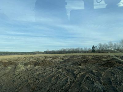 Fotografi av en speilende overflate (sannsynligvis vann eller våt asfalt) som reflekterer himmelen, trær og bakken.