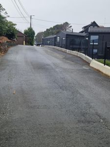 Fotografi av en nyasfaltert vei eller gate med en mørk fasadet hus i bakgrunnen.