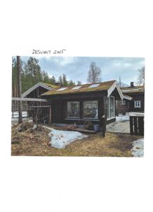 Fotografi av en hytte med grønt tak og solceller, tatt i vinterforhold med snø på bakken.