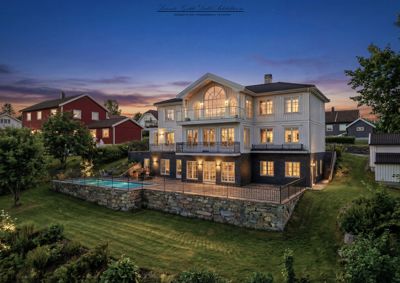 Fotografi av en villa med utepool, sett fra et høyere nivå mot en solnedgang.