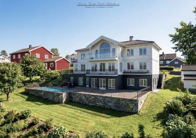 Fotografi av en hvit villa med svarte sokler og en svømmebasseng i bakgården.