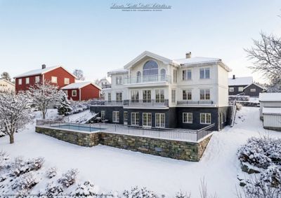 Fotografi av en hvit og mørk villa med snødekke, sett fra siden/bak i et nabolag.