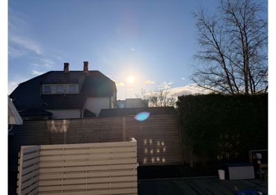 Fotografi av en bolig sett fra bakgården, med solen som skinner bak huset.