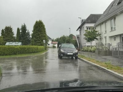 Fotografi av en bilparkert på en gate i et boligområde, sett fra kjøretøy.