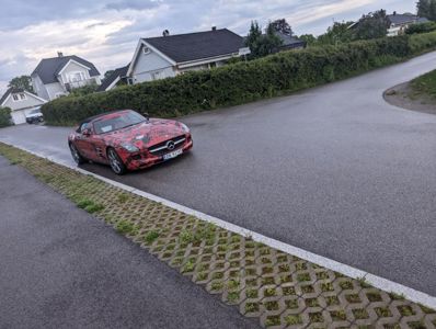 Fotografi av en rød Mercedes-bil som kjører på en asfaltert vei i et boligområde.