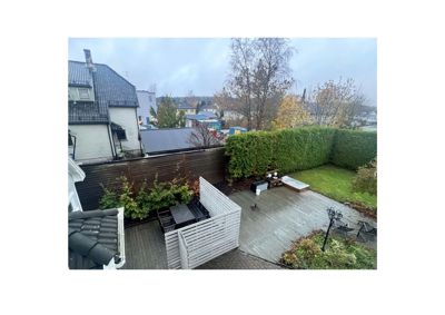 Fotografi av en bakgård med terrasse, hegn, hage og nabolag.