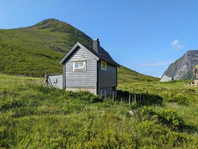 Fotografi av en liten hytte i et grønt, fjellaktig landskap.
