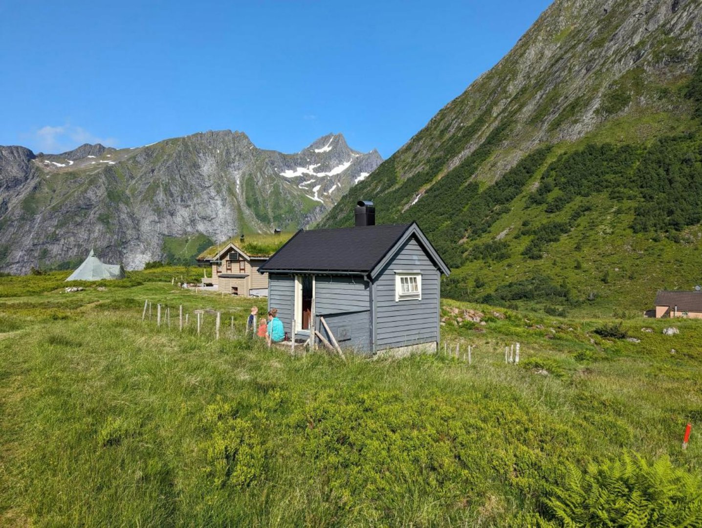 Fotografi av en liten hytte i et fjellandskap med to personer foran.