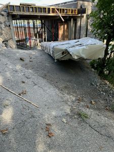 Fotografi av en byggeplass med en delvis ferdig bygning i bakgrunnen, en stor pakke materialer i forgrunnen og en steinvegg.