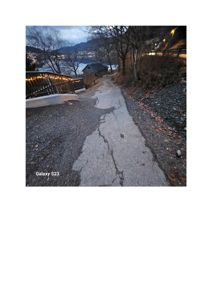 Fotografi av en krakket asfaltert vei eller sti som går nedover mot en by i bakgrunnen.