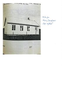 Et svart-hvitt fotografi av en liten, hvit bygning med et skrått tak og flere vinduer. Bildet har håndskrevne notater på siden.