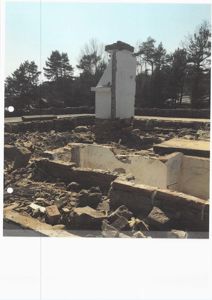 Fotografi av en bygning i ruiner eller under riving, med synlig fundament og skorstein.