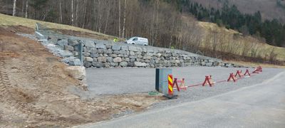 Fotografi av en byggeplass som viser en nybygd steinmur, en grusbelagt overflate og en vei i bakgrunnen.