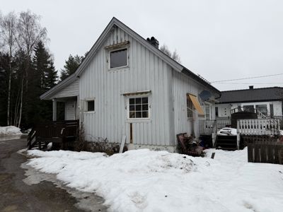 Fotografi av en hvit, trepanelert enebolig sett fra siden. Bildet viser fasaden, vinduer, en veranda, en satellittantenne og snø på bakken.