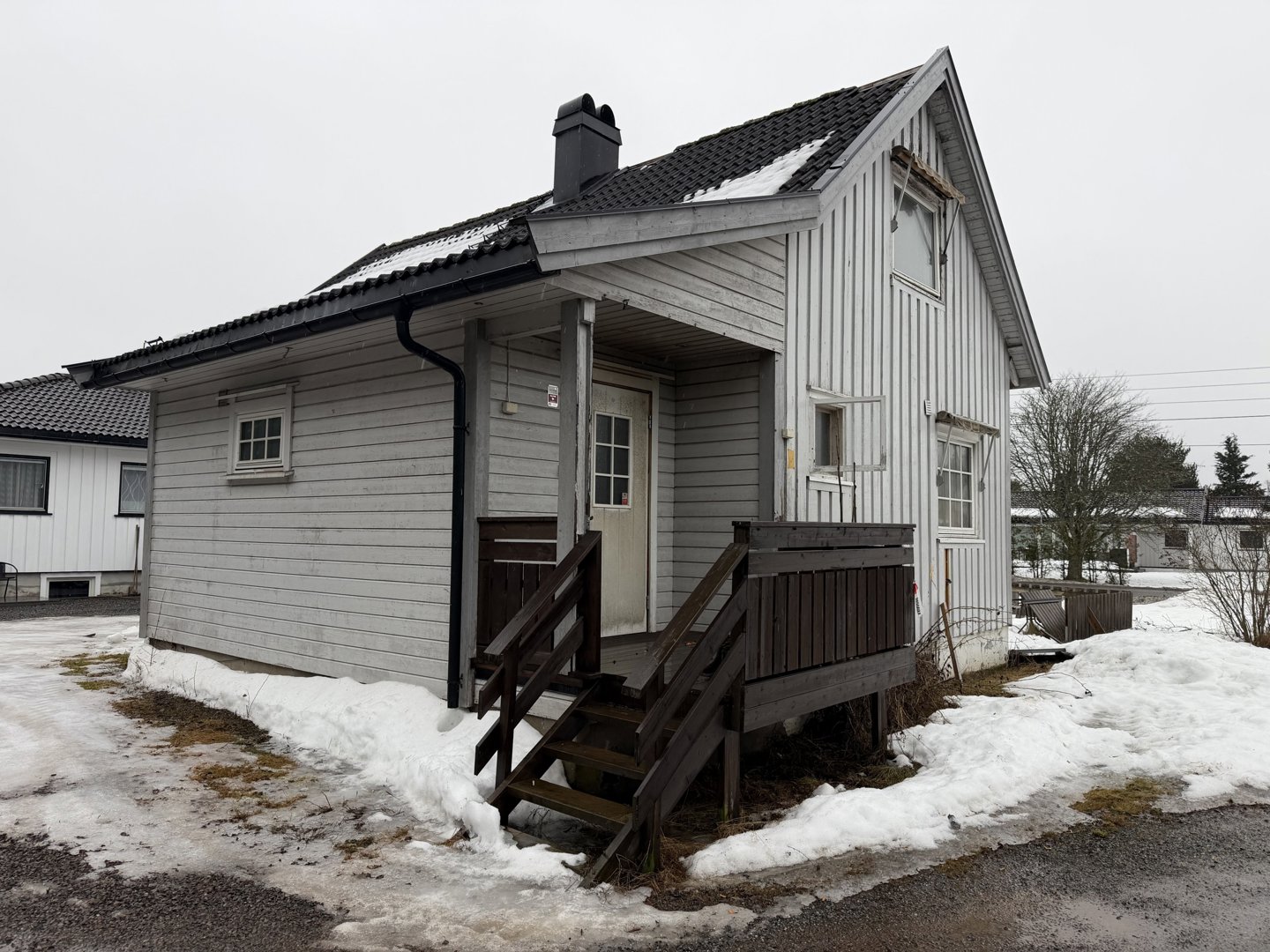 Fotografi av en liten, hvitfarget trehytte med snø på bakken og taket.