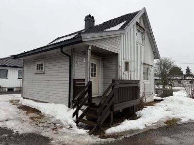 Fotografi av en liten, hvitfarget trehytte med snø på bakken og taket.