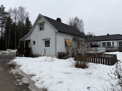 Fotografi av en hvit, trepanelert enebolig med mørk takflate, sett fra siden. Det er snø på bakken og en tilhørende bygning i bakgrunnen.