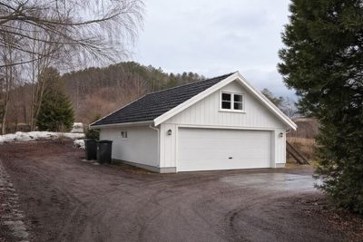 Fotografi av en hvit garasje med svart tak, sett fra utsiden.