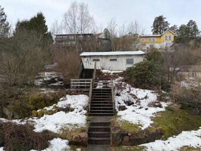 Fotografi av en uteplass med trapper, en hvit uthusbygning og nabolagshus i bakgrunnen.