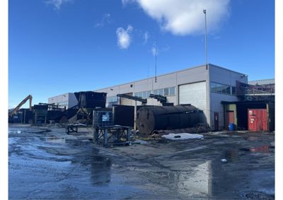 Fotografi av en industribygning sett fra utsiden, med utstyr og materialer på plassen foran.