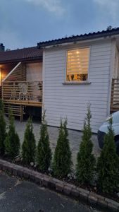 Fotografi av en hvitbeidlet hytte eller bolig med etasjehus, terrasse og hageanlegg.