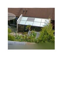 Fotografi av en utvendig tilføyelse til en bygning, sannsynligvis en glassveranda eller solrom, sett fra en høyere vinkel.