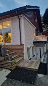 Fotografi av en ferdig eller nesten ferdig bygning sett fra siden, med fokus på fasade, trapp og inngang.