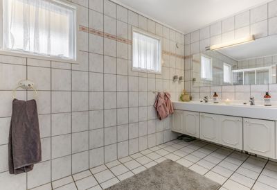 Fotografi av et innredet bad med flisvegger, toalett, vask og vinduer.