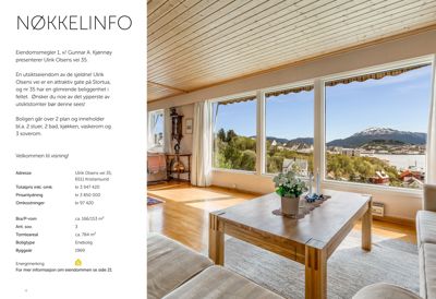 Fotografi av et interiør i en bolig, med utsikt over en fjord og fjell fra vinduet.