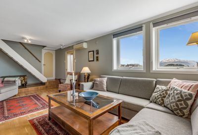 Fotografi av et innredet stueområde med sofa, bord og vinduer.