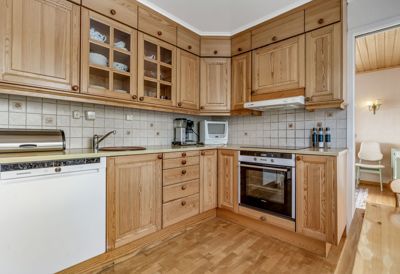 Fotografi av en kjøkkeninnredning med trekabinetter, hvite fliser på veggen og parkettgulv.