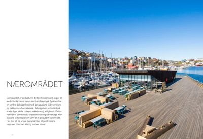 Fotografi av et moderne bygg med uteplass ved en kai, med båtmerke i bakgrunnen.