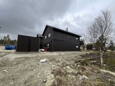 Fotografi av en nybygd, mørk trehus i en byggeplass under grå himmel.