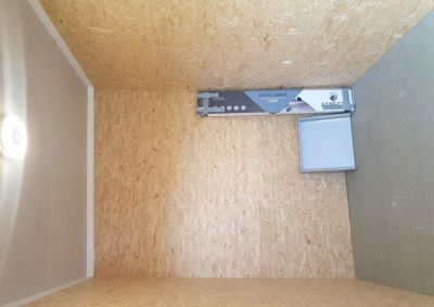 Fotografi av en tom rominnvendig vinkel i en bygning under oppføring, med OSB-gulv og vegger.