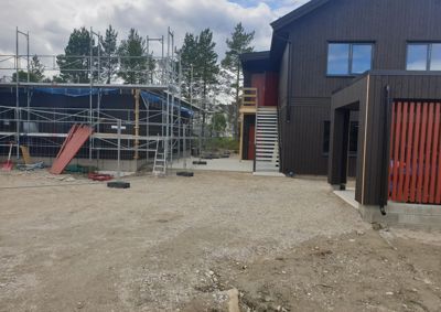 Fotografi av en byggeplass med en ferdigbeveget fasade til høyre og en bygning under oppføring med stålramme og trelast til venstre.