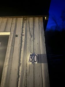 Fotografi av en fasade med tømmerpanel, et husnummer (30) og en dør.