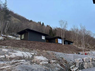 Fotografi av en moderne, mørk bygning i ferdigstillelse eller nybygd, plassert på en bratt, skogkledt bakke.